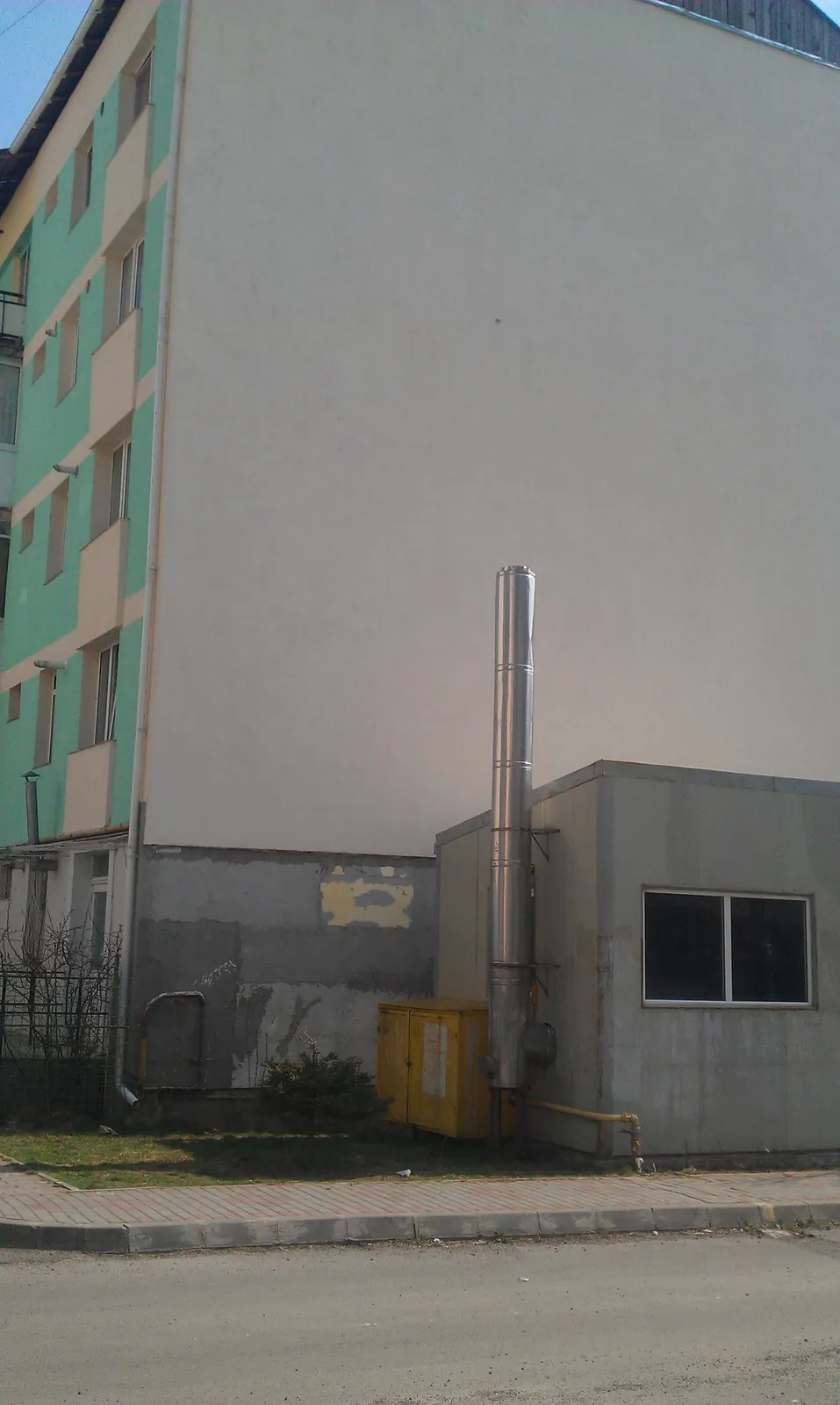 Coșul de fum metalic al unei centrale termice lipite de un bloc, mult mai scund decât clădirea