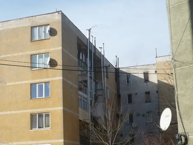 Fațadă de bloc cu numeroase coșuri de fum metalice montate pe perete, de la cazanele apartamentelor