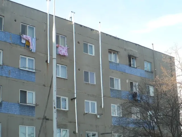Fațadă de bloc cu mai multe coșuri de fum metalice albe care urcă pe exterior până deasupra acoperișului