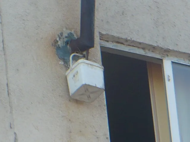 Găleată de plastic agățată de coșul de fum, lângă o fereastră deschisă