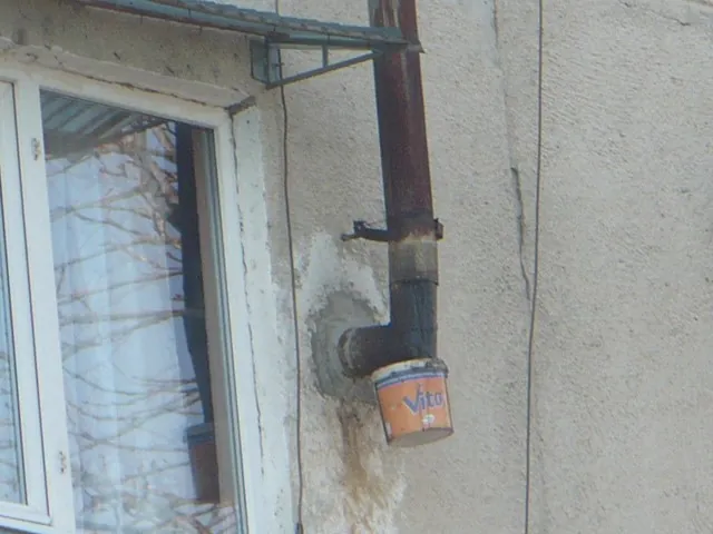 Găleată agățată sub cotul unui coș de fum ruginit, lângă o fereastră