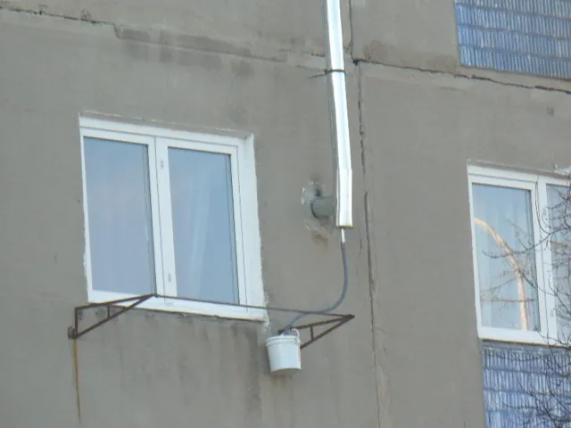 Coș de fum cu un furtun pentru condens care coboară într-o găleată pusă pe un suport sub fereastră