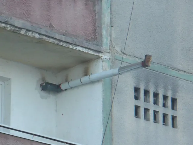 Coș de fum scurt care iese oblic din perete, sub un balcon, lângă un perete înnegrit