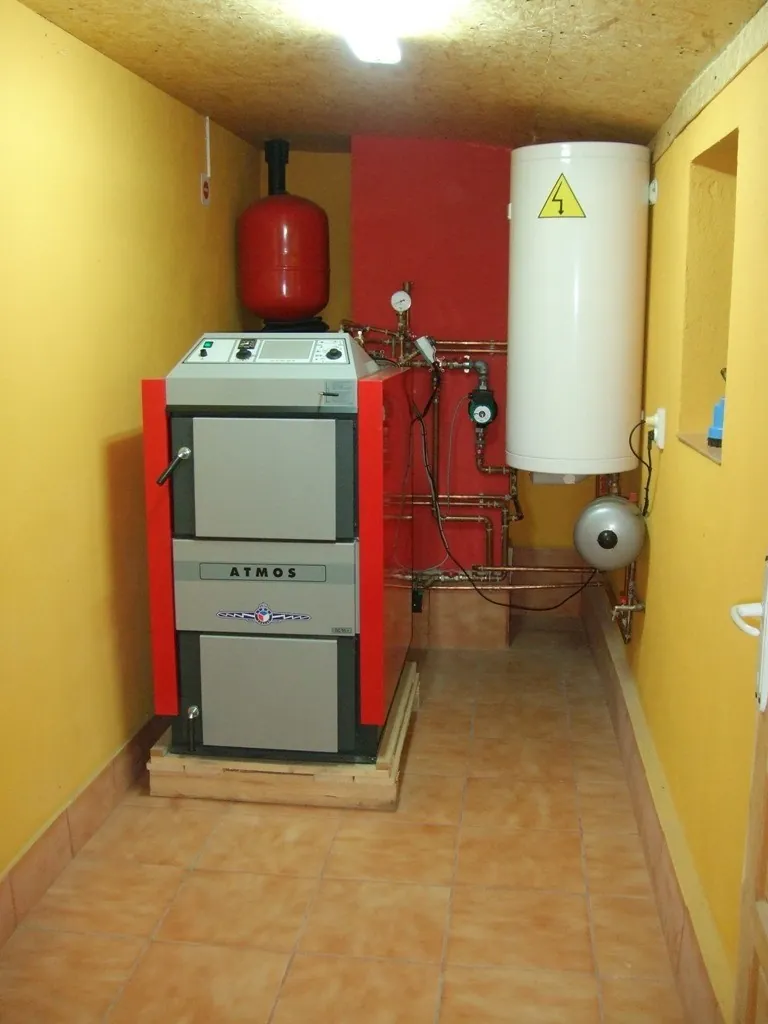 Cazan pe combustibil solid așezat pe un cadru din lemn, într-o cameră cu gresie