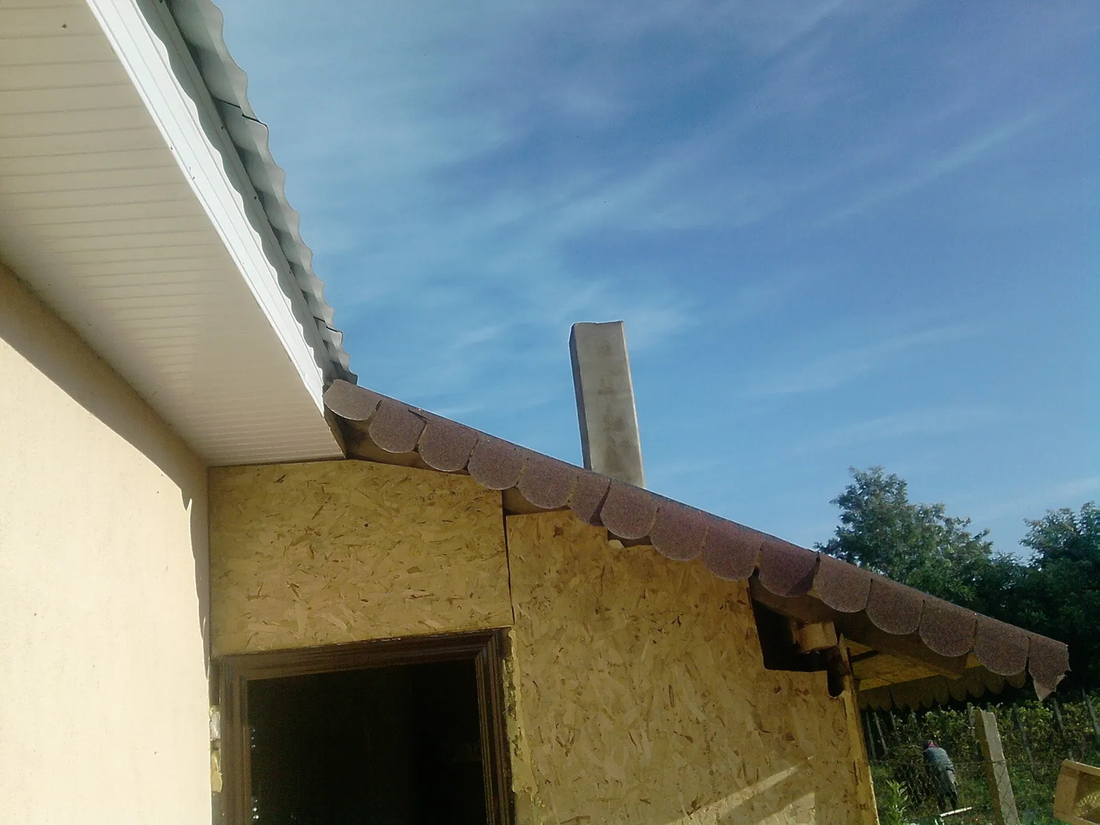 Camera centralei termice văzută din exterior, o construcție din plăci de lemn cu coșul de fum lângă perete