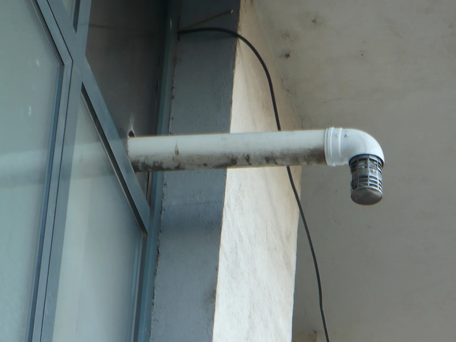 Conducte concentrice cu cot la 90 de grade și terminal orientat în jos, lângă o fereastră