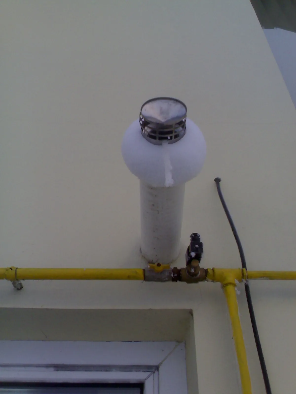 Terminal de evacuare vertical acoperit cu gheață, deasupra unei conducte de gaz galbene