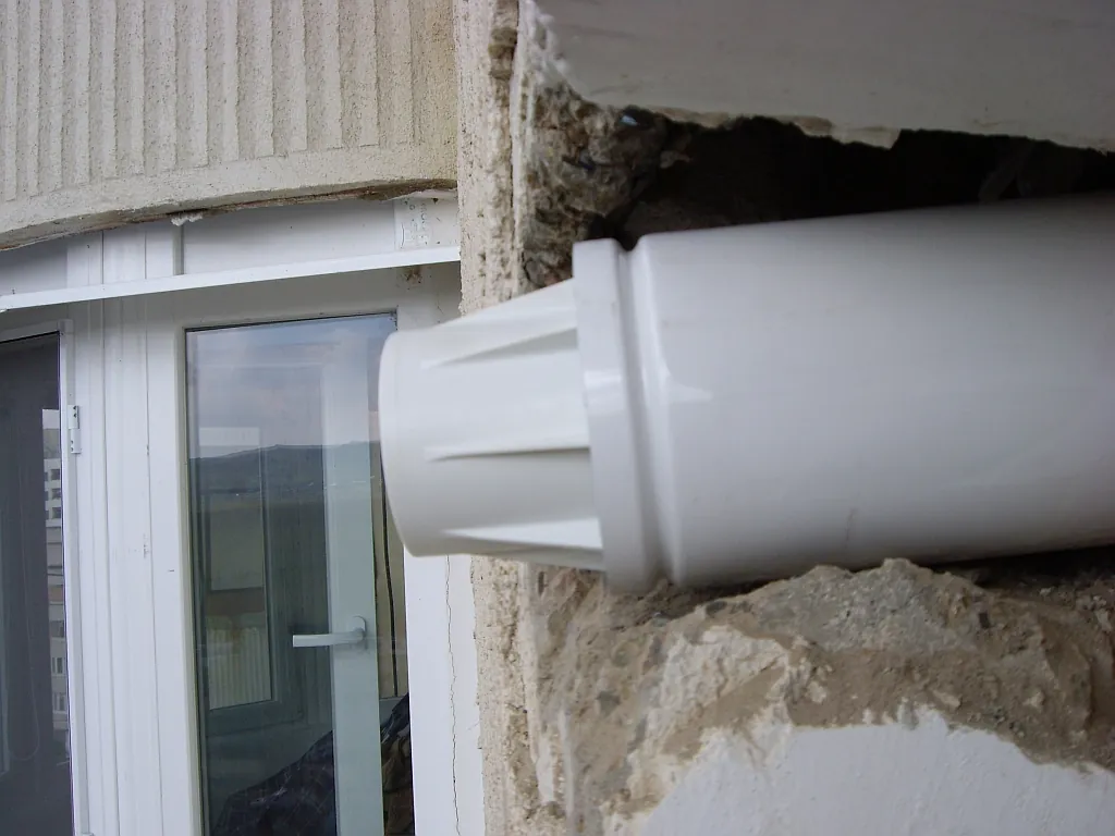 Conductă concentrică care nu iese complet din perete, lângă o ușă de balcon