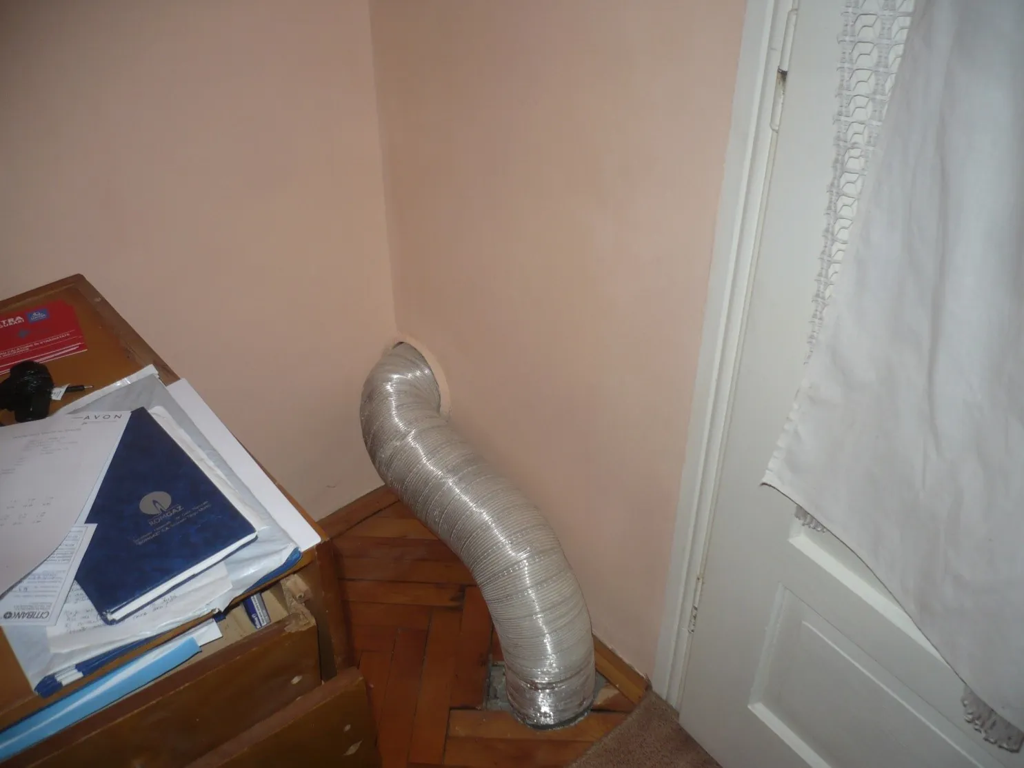 Tub flexibil din aluminiu folosit drept coș de fum, care trece prin parchetul unui dormitor